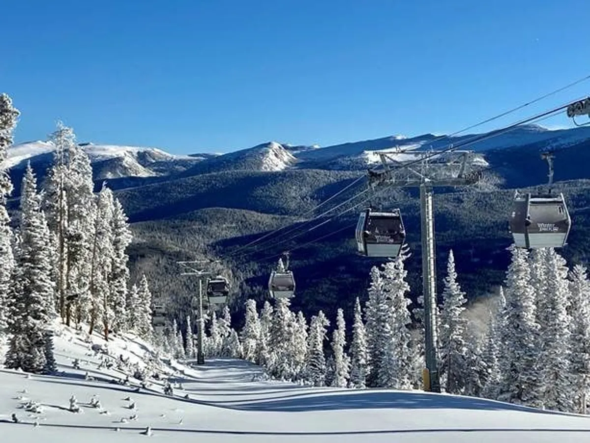 This scenic exterior shot captures gondolas gliding against a backdrop of snow-covered trees and a mountain range, evoking the excitement of nearby Winter Park Resort's activities like skiing, snow tubing, and hiking.