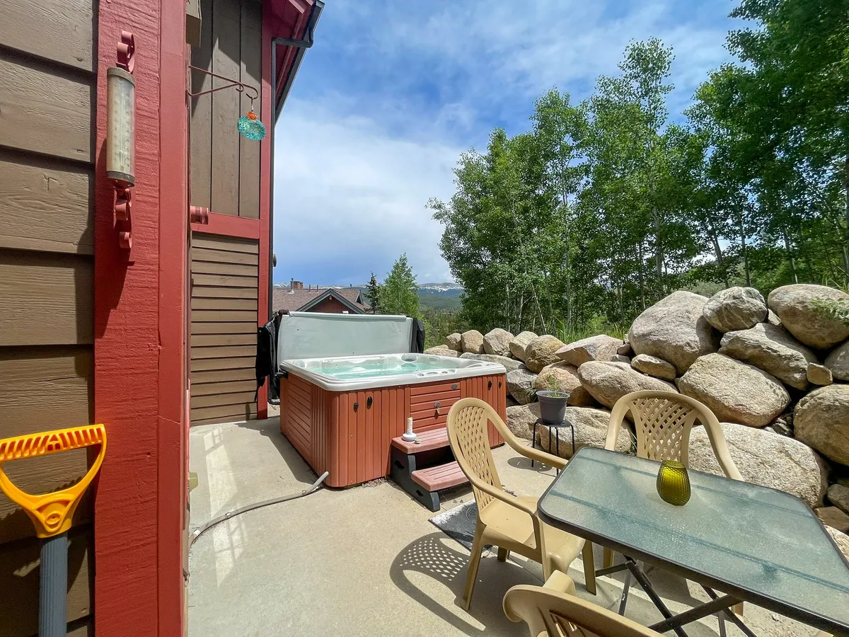 This exterior image features a private hot tub surrounded by natural greenery, outdoor seating, and a rock wall, creating a tranquil environment ideal for family relaxation after a day of adventures. The space is inviting and perfect for evening gatherings or morning coffee outdoors.