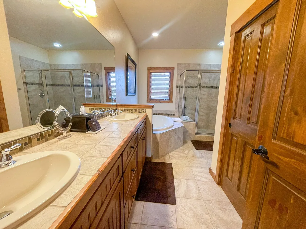 A serene, spa-inspired bathroom with a double sink vanity, a large soaking bathtub, a glass shower enclosure, and wooden accents. The space exudes a calming, rejuvenating atmosphere reminiscent of a luxury hotel.