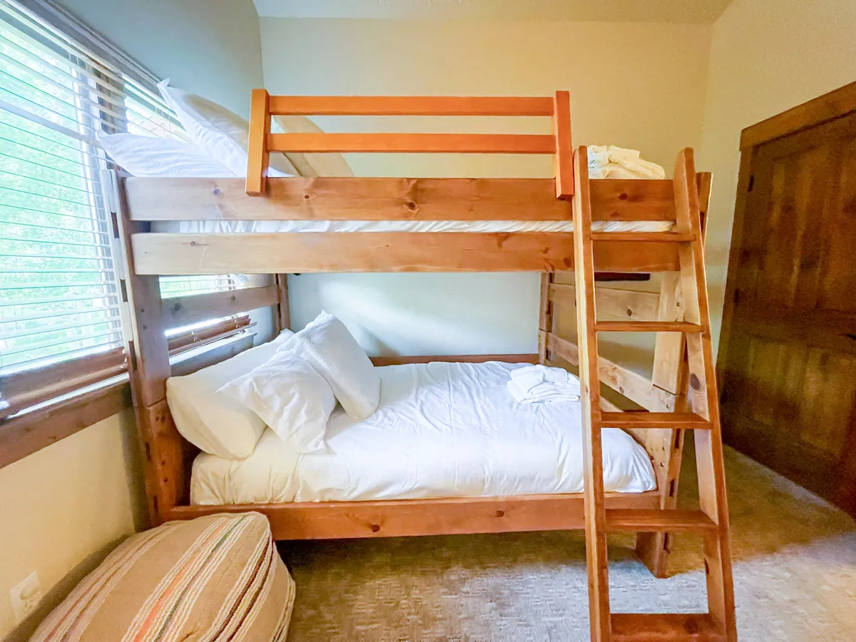 A cheerful bunk room with a full-over-full bunk bed, soft pillows, and a sturdy ladder. The inviting space is full of natural morning light, perfect for reading, playing, or building blanket forts—an ideal haven for kids or friends.